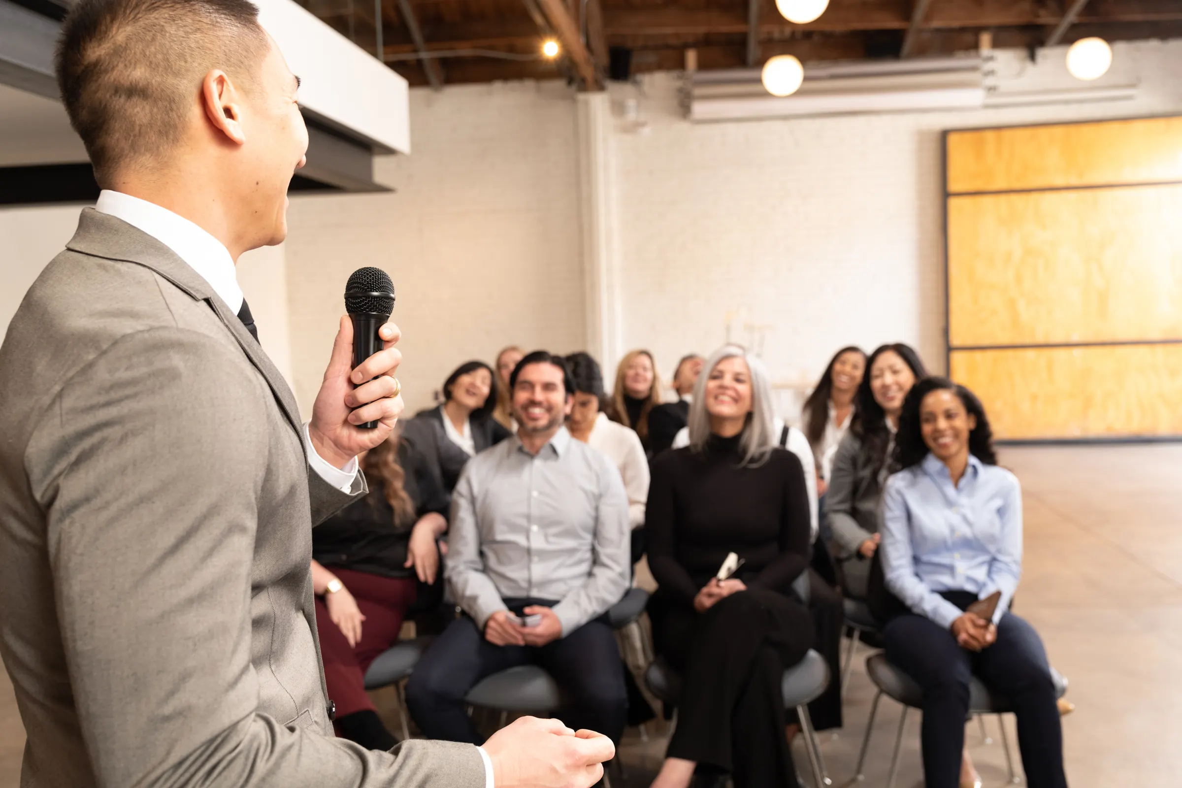 A Toastmasters member speaks with a microphone to a smiling, attentive audience