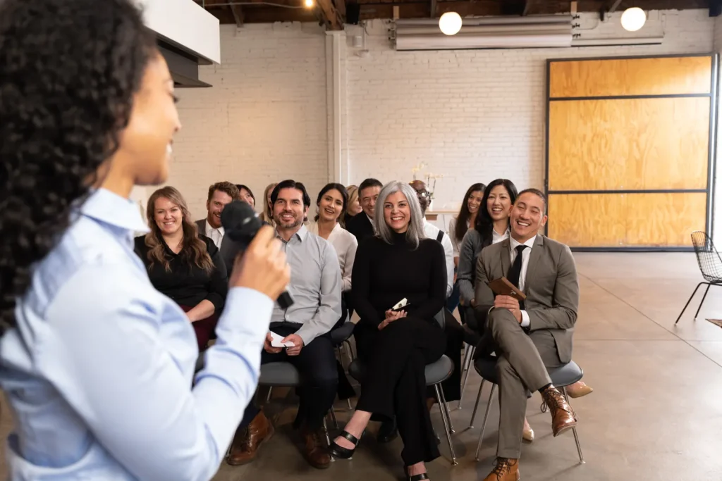 A speaker holding a microphone makes the audience laugh at a Toastmasters meeting